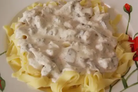 Pyszny makaron z kurczakiem i pieczarkami w kremowym sosie, podany na talerzu z motywem maków.