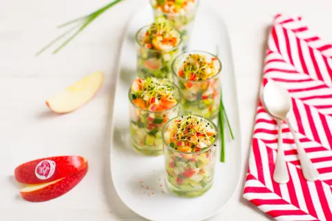 Amuse-bouche pomme et crevettes dans des verrines, garnies de pousses. Des quartiers de pomme Pink Lady sont disposés à côté.