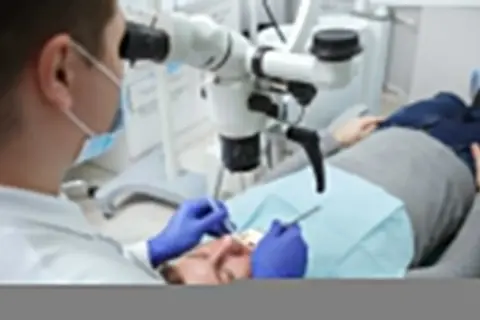 Dentysta pod mikroskopem bada ząb pacjenta. Po leczeniu kanałowym można jeść, ale warto poczekać na znieczulenie.