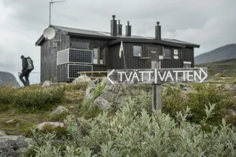 Vandrare närmar sig en av kungsleden stugor. En skylt pekar mot "TVÄTT VATTEN".