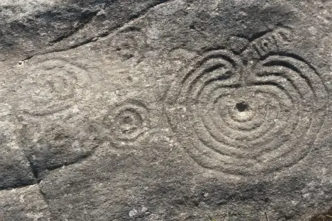 Petroglifos de Mogor: grabados circulares concéntricos y un posible sol en una roca antigua.