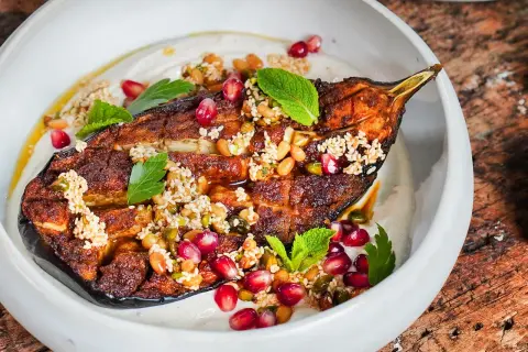 Gebackene Aubergine mit Tahini, Granatapfelkernen und Minze. Ein köstliches Gericht, das zeigt, wie vielseitig auberginen rezepte im backofen sein können.