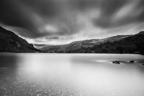 Un photographe paysage capture un lac paisible sous un ciel dramatique, les montagnes se reflétant dans l'eau lisse.