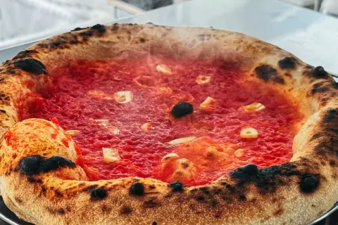 Eine dampfende Pizza Marinara mit knusprigem Rand und roten Tomaten.