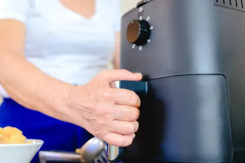 Dłoń osoby wyciąga szufladę frytkownicy beztłuszczowej, pokazując, jak działa air fryer.