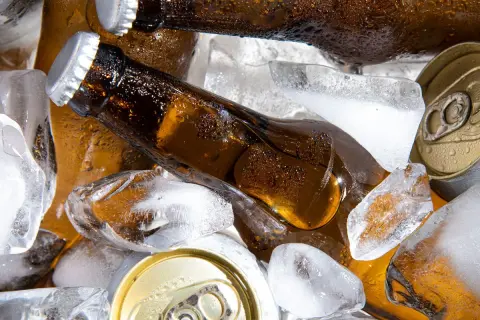 Chłodne piwo w butelkach i puszkach wśród kostek lodu. Szukasz piwa alkoholowego, które ma najmniej kcal?
