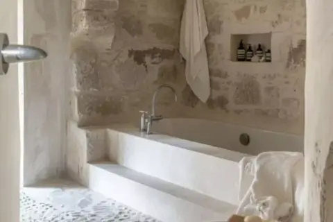 Bain relaxant dans une **salle de bain méditerranéenne** aux murs de pierre brute. Serviette blanche suspendue, robinetterie moderne.