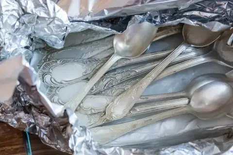 Stare, ozdobne łyżki i widelce owinięte w folię aluminiową, gotowe do czyszczenia srebra.