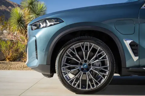 Nowe BMW X5 2023 w kolorze niebiesko-zielonym, z felgami o skomplikowanym wzorze, zaparkowane na tle pustynnego krajobrazu.