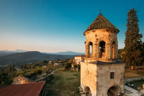 Wieża dzwonnicza Gelati Monastery na tle górskiego krajobrazu o zachodzie słońca.