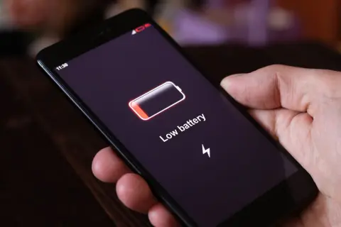 Dłoń trzyma smartfon z ikoną niskiego poziomu baterii i napisem "Low battery". Funkcja always on display pokazuje godzinę 11:30.