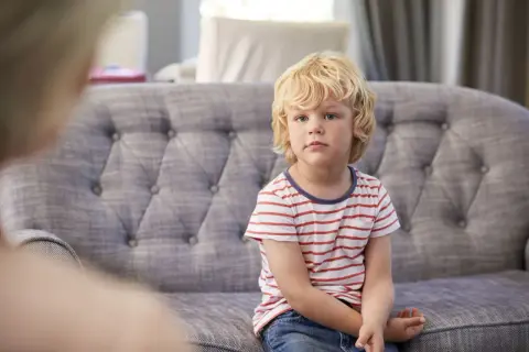 Chłopiec z blond włosami siedzi na kanapie w paski.