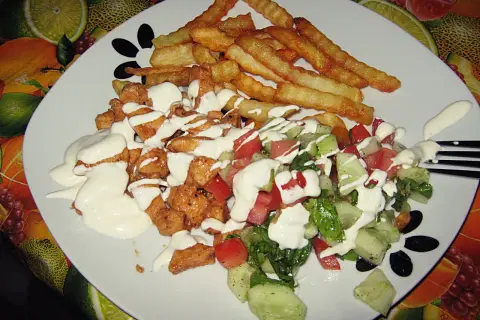 Pyszny kebab na talerzu z chrupiącymi frytkami i świeżą sałatką, polany kremowym sosem.