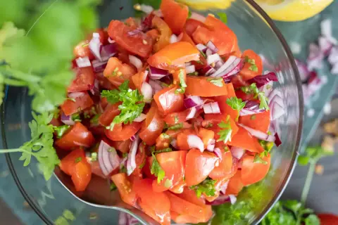 Frischer tomatensalat mit zwiebeln und Petersilie in einer Glasschüssel, garniert mit Koriander.