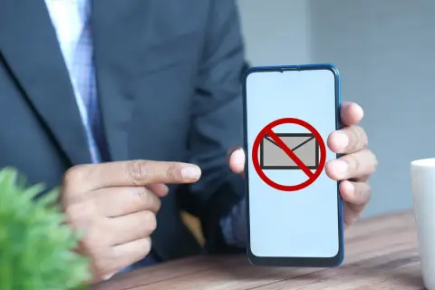 Hombre señala un teléfono con un símbolo de "no" sobre un sobre. Parece que no me llegan los sms.