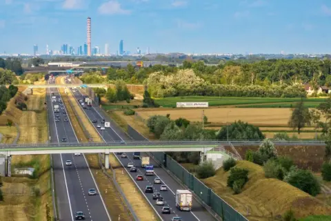 Autostrada z ruchem samochodowym i widokiem na miasto w tle.