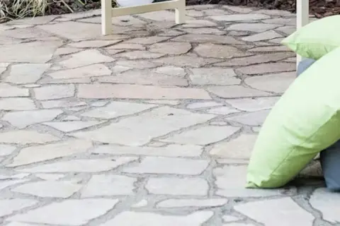 Naturalny chodnik z płyt chodnikowych, idealny do relaksu na świeżym powietrzu. Dwie poduszki, jedna jasnozielona, dodają koloru.