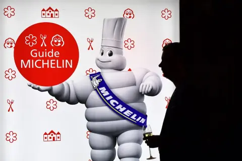 El muñeco Michelin, con su banda "MICHELIN", posa junto a un hombre con copa. Un símbolo de los restaurantes con estrella Michelin.