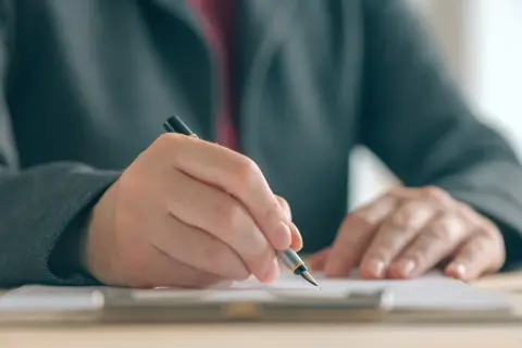 Dłoń w garniturze pisze piórem na dokumencie, co symbolizuje postępowanie egzekucyjne w administracji.