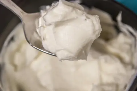 Un cucchiaio raccoglie una generosa porzione di cremoso yogurt greco fatto in casa, pronto per essere gustato.