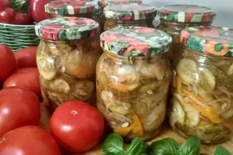 Słoiki z ogórkami w zalewie gyros, obok pomidory i bazylia.