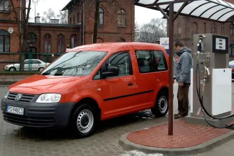Pomarańczowy Volkswagen Caddy, auto zasilane CNG i hybrydą, tankuje na stacji.