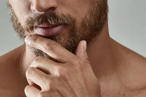 Gros plan sur un homme pensif, sa main caressant sa barbe. L'évolution de sa barbe, de la naissance à sa forme actuelle, est visible.