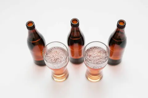 Tre bicchieri di birra con schiuma e quattro bottiglie marroni vuote, una birra andata a male.