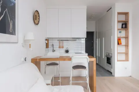 Interiores de casas sencillas con cocina blanca, barra de madera y sofá blanco. Estilo minimalista y funcional.