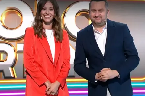 Uśmiechnięta kobieta w czerwonej marynarce i mężczyzna w granatowym garniturze na tle logo "Koło Fortuny".