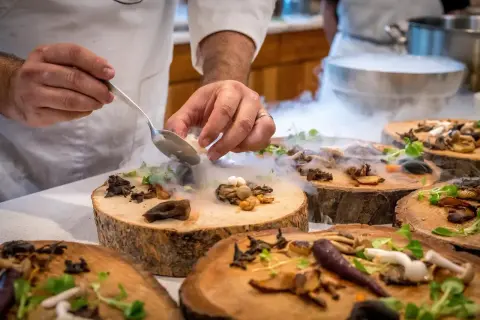 Szef kuchni serwuje danie z grzybów i ziół na drewnianych plastrach, tworząc magiczną atmosferę. To uczta godna najlepszych restauracji w Warszawie.