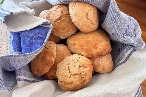 En hög med gyllene, luftiga scones som vilar i en blåvitrandig kökshandduk. Perfekt för fikat!