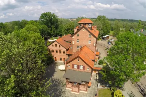 Hotel Młyn Elbląg, ceglane budynki z czerwonymi dachami, otoczone zielenią.