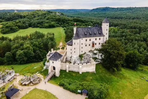 Malowniczy zamek Bobolice, wzniesiony na skale, otoczony zielonymi lasami i polami.