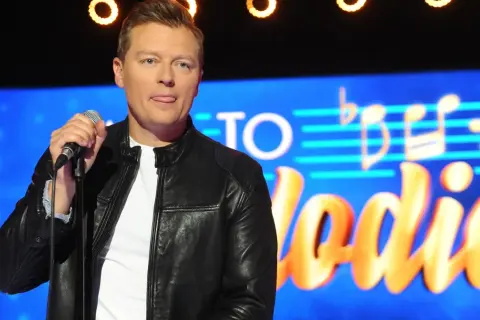 Artysta z wyciągniętym językiem trzyma mikrofon na tle napisu "Jaka to melodia". Czyżby zapowiadał największe zmiany w regulaminie?