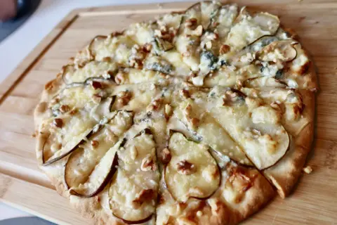 En utsökt pizza med päron, valnötter och krämig gorgonzola på en träskärbräda.