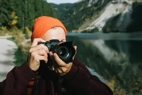 Osoba w pomarańczowej czapce robi zdjęcie aparatem, który mógłby być Nikon D7000. Dane techniczne tego modelu pozwalają na uchwycenie piękna górskiego krajobrazu.