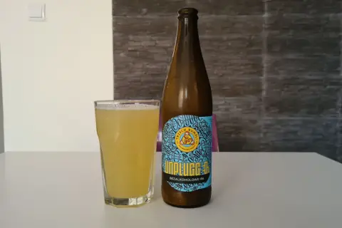 Szklanka i butelka piwa miodowego bezalkoholowego Unplugged IPA na białym stole.