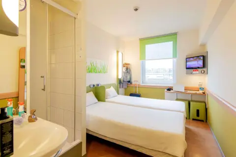 Pokój w hotelu Ibis z dwoma łóżkami, łazienką, biurkiem z laptopem i telewizorem.