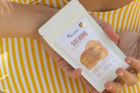 Une main tient un paquet de "Solaire Bronzage" de Valebio, suggérant une peau protégée et hâlée.