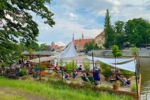 Entspannte Atmosphäre an einem Flussufer-Café in Breslau. Ein perfekter Ort für Breslau Geheimtipps, mit Liegestühlen und Sonnensegeln.