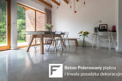 Nowoczesne wnętrze z betonem polerowanym na podłodze. Stół, krzesła, biurko i okna z widokiem na ogród.
