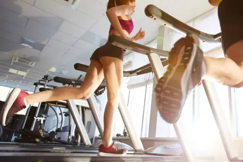 Due persone corrono sui tapis roulant in palestra. Nonostante correre fa venire la cellulite, loro si allenano con determinazione.