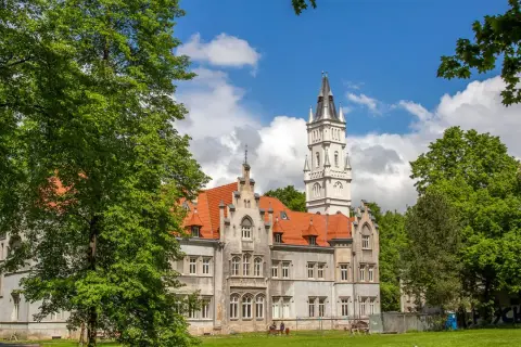 Pałac w Nakle Śląskim otoczony zielenią, z charakterystyczną wieżą i czerwonym dachem.