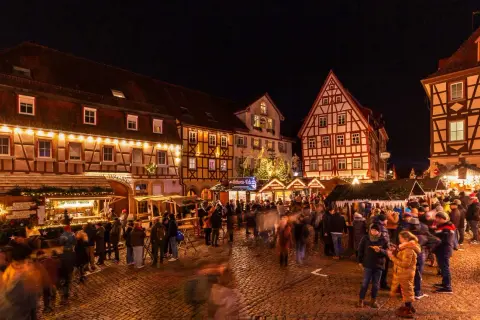 Bunte Lichter und geschäftiges Treiben auf dem **Bad Wimpfen Weihnachtsmarkt**. Fachwerkhäuser und Buden laden zum Verweilen ein.