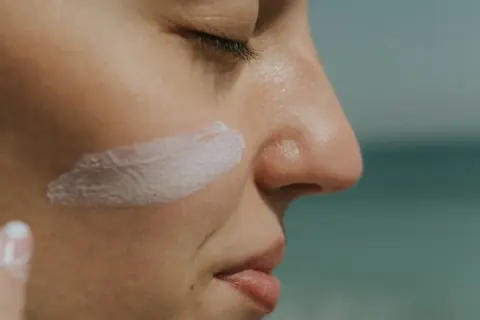 Aplicando crema solar biodegradable en la mejilla, protegiendo la piel del sol.
