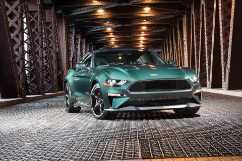 En grön pony car, en Ford Mustang, står på ett gallergolv under en bro med belysning.