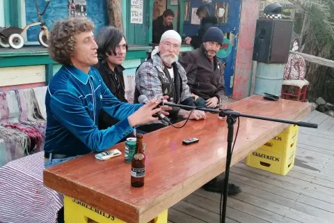 Hombres sentados en una mesa de madera en el bar de Joe Cabo de Gata, con micrófonos y botellas de cerveza.