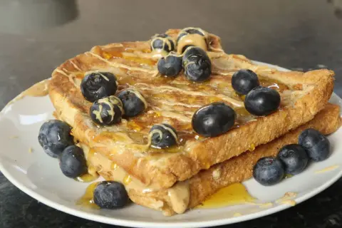 Goldbrauner French Toast Protein-Stapel mit Erdnussbutter, Honig und Blaubeeren.