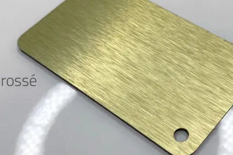 Échantillon de **dibond or brossé** avec une finition texturée et un trou percé.